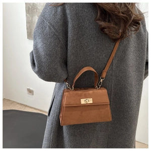 Brown frosted leather crossbody bag featuring a golden square twist lock on a beige coat