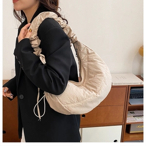Detalle de un bolso hobo acolchado beige con correa fruncida y diseño de media luna