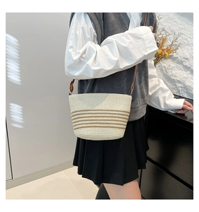 Close-up of a woven cream bucket bag with brown stripes and a leather shoulder strap