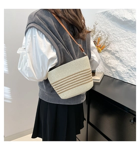 Rear view of a woven bucket bag with brown stripes and leather shoulder strap on a model