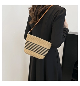 Detail of woven straw tote bag with black horizontal stripes and brown leather strap