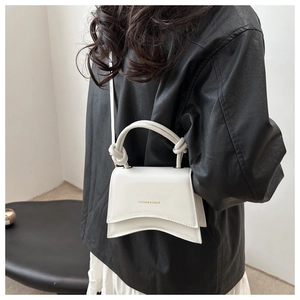 Detail of white structured handbag with curved base and gold lettering on black jacket