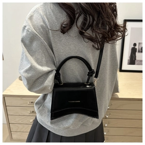 Close-up of black leather handbag with curved bottom and golden text detail