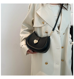 Detail of a black saddle crossbody bag with a gold heart buckle on a white trench coat