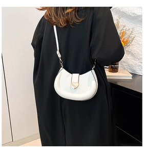 Detail of white half-moon bag featuring gold heart buckle and adjustable strap on black coat