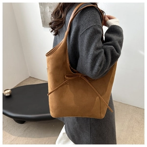 Detail of a brown suede tote bag with a decorative ribbon bow and contrast straps