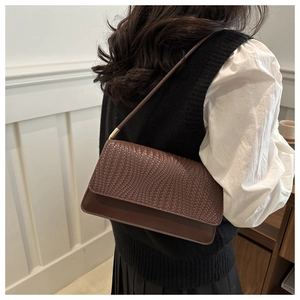 Detail of dark brown woven texture shoulder bag worn by model in a cozy indoor setting