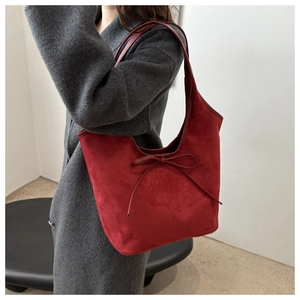Detail view of large red suede tote bag with bow accent worn over a grey coat