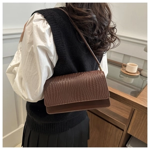 Detailed view of woven texture and gold metal hardware on a brown leather shoulder bag