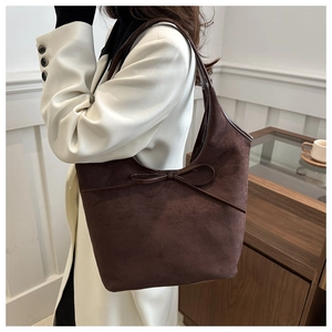 Detail of dark coffee suede tote bag with delicate leather bow on model's shoulder