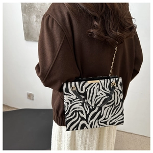 Detail of zebra pattern crossbody bag with gold chain strap on an elegant model outfit