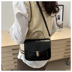 Detail of minimalist black crossbody bag with gold buckle worn by model in a cozy room