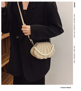 Close-up of golden shell bag with pearl handle and metallic pleated texture on black blazer