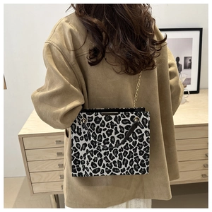 Detail of leopard print handbag featuring a black handle and gold chain strap on model