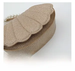 Detail of champagne shell-shaped woven clutch bag with white pearl strap and metallic texture