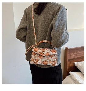Detailed side view of orange and grey snakeskin pattern crossbody bag on a model