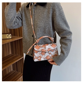 Close-up of orange and white snakeskin pattern bag with woven handle on retro shelf