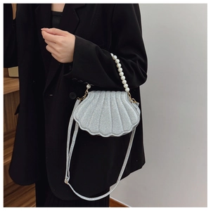 Fashionable shell-shaped bag with silver sequins and pearl handle shown on a model