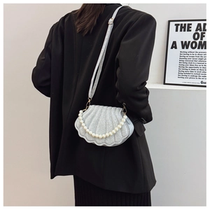 Macro view of shell-shaped silver glitter bag with pearl handle and pleated texture