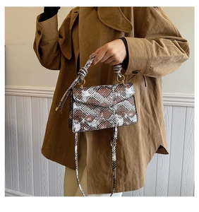 Detail of faux leather snake print crossbody bag with knotted handle and gold hardware