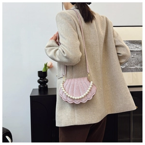 Detail of pink shell-shaped crossbody bag with pearl handle and golden hardware on model