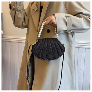 Close-up of black glitter shell bag with white faux pearl handle on model in trench coat