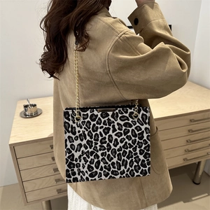 Leopard print crossbody bag with gold chain strap shown on model's shoulder in beige coat