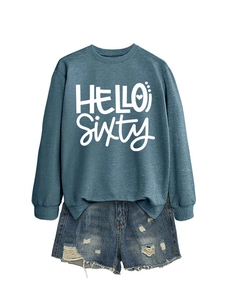 Detalle de sudadera verde azulado con texto Hello Sixty blanco y shorts vaqueros