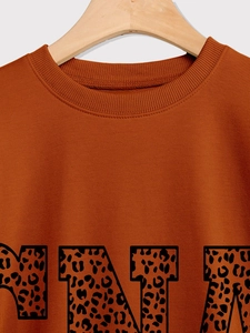 Detailed view of caramel orange sweatshirt featuring leopard print MIA lettering and ribbed neck