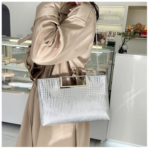 Silver crocodile texture handbag with metal handle and chain strap worn by a model