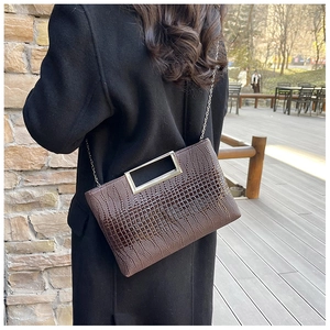 Close-up of brown croc-effect clutch with silver metal handle on a black coat