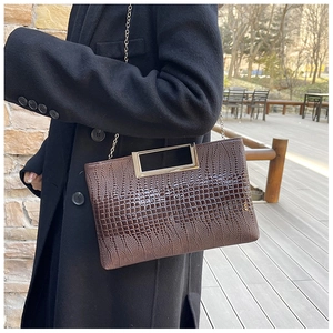 Detail of brown crocodile pattern handbag with silver metal handle and chain strap