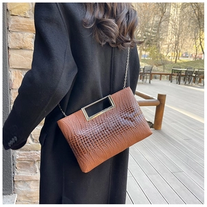 Detail of caramel brown crocodile texture handbag with silver metal handle and chain strap