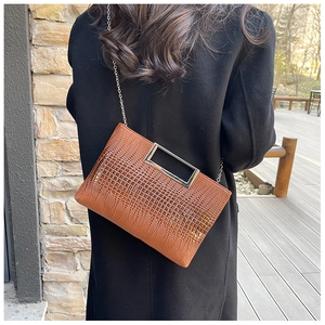 Brown crocodile embossed handbag with metallic handles and chain strap on street model