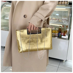Detail view of metallic gold crocodile texture clutch with handle and chain strap