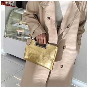 Detail of gold crocodile pattern handbag with silver metal handle and chain strap