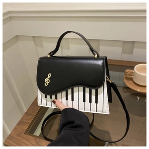 Détail du sac à main motif touches de piano avec clé de sol dorée sur une table