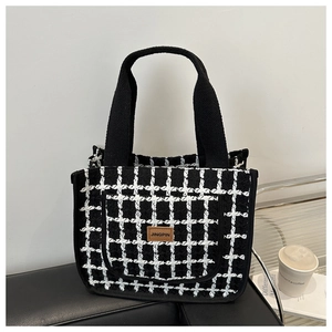 Detail of black and white plaid tweed tote bag with a brown leather logo on a seat