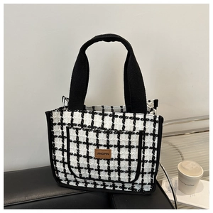 Detail of checkered tweed tote bag with a leather patch and dual handles on a black bench