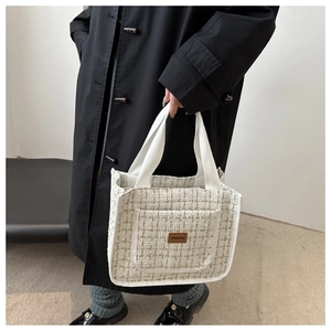Detail of off-white tweed tote bag featuring a leather logo patch and woven texture