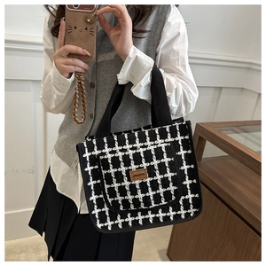 Detail of black and white checkered fabric tote bag with brown leather brand label
