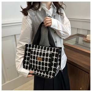 Detail of checkered tote bag with woven texture, leather logo tag and sturdy canvas handles