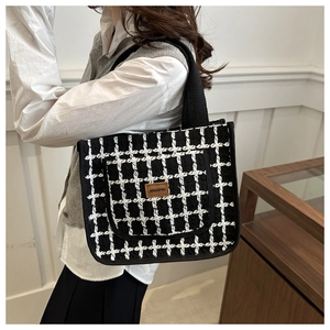 Detail shot of a black and white checkered tweed tote bag with a brown leather patch label