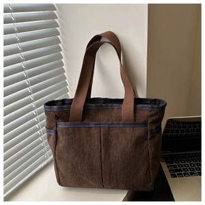 Detailed view of corduroy tote bag with multiple pockets and striped trim in soft light