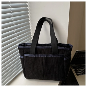 Macro detail of black corduroy tote bag showing striped texture and front storage pocket