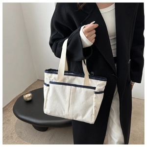 Close-up of off-white corduroy tote bag with blue trim and multiple front pockets