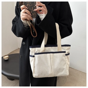Detail of white corduroy tote bag with blue trim and multiple large storage pockets