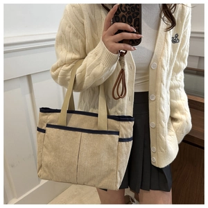 Detail view of beige corduroy tote bag with multiple pockets and navy blue trim detail