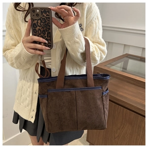 Detail of a brown corduroy tote bag featuring multi-pocket design and contrast blue piping