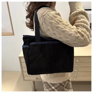 Detail of black corduroy tote bag with blue trim shown on model in cozy interior